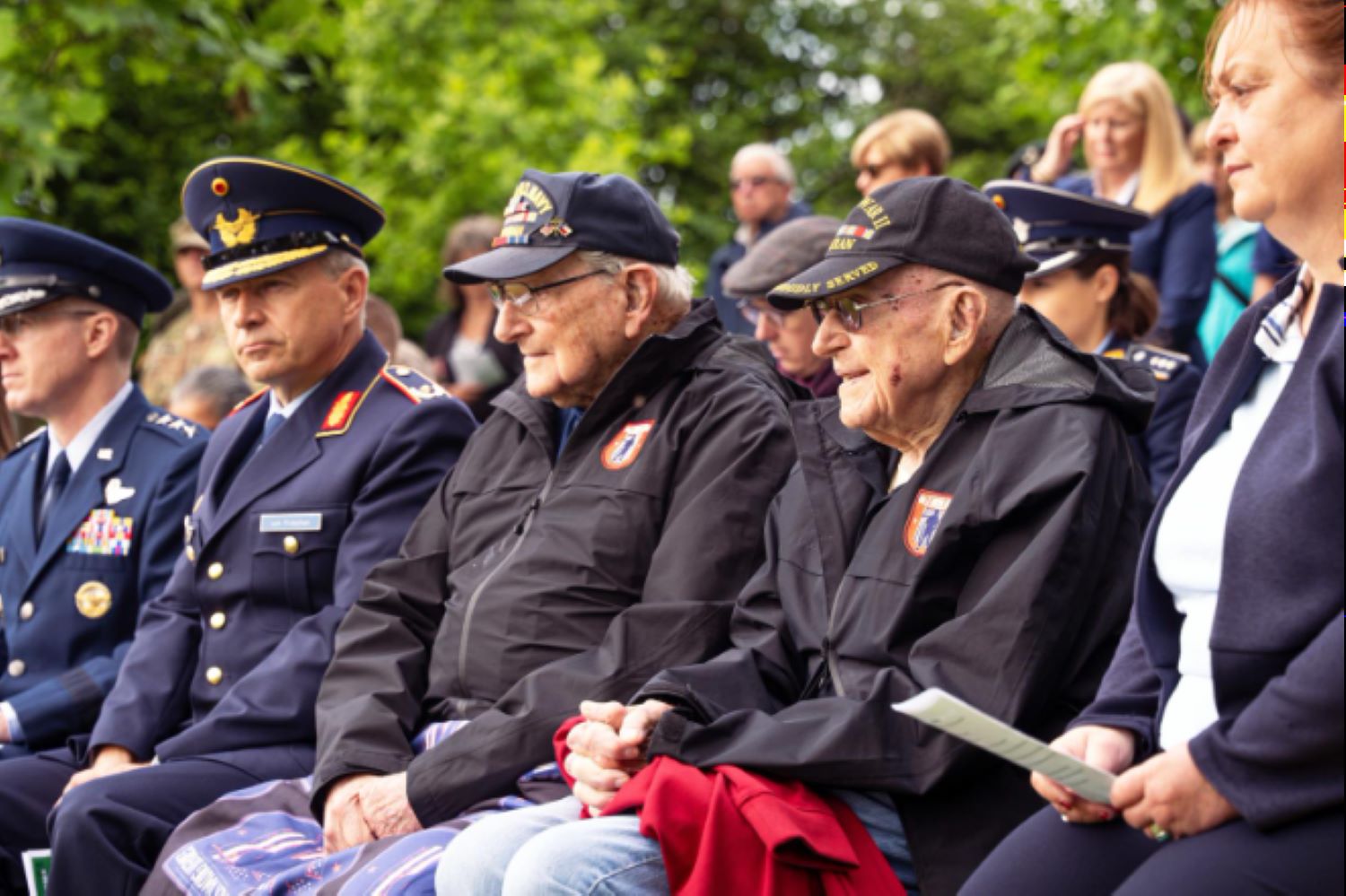 A row of elderly World War II veterans—dressed in matching black jackets and hats