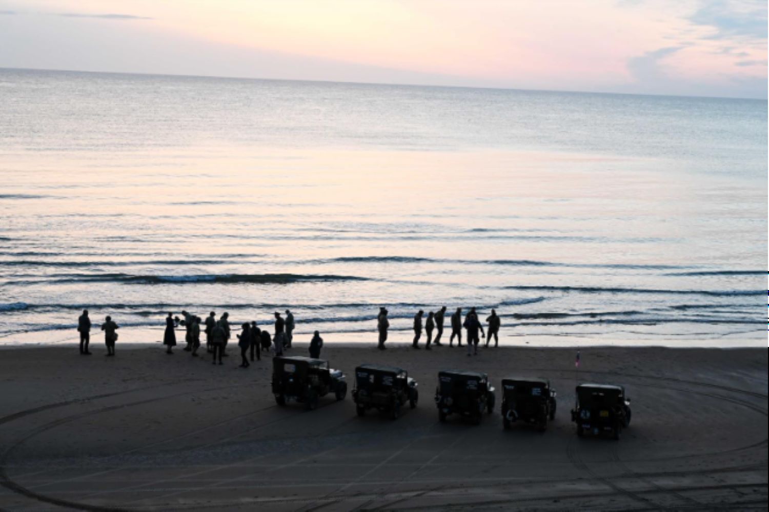 Historical reenactors, dressed in World War II-era U.S. military uniforms, stand near the shoreline in Vierville-sur-Mer