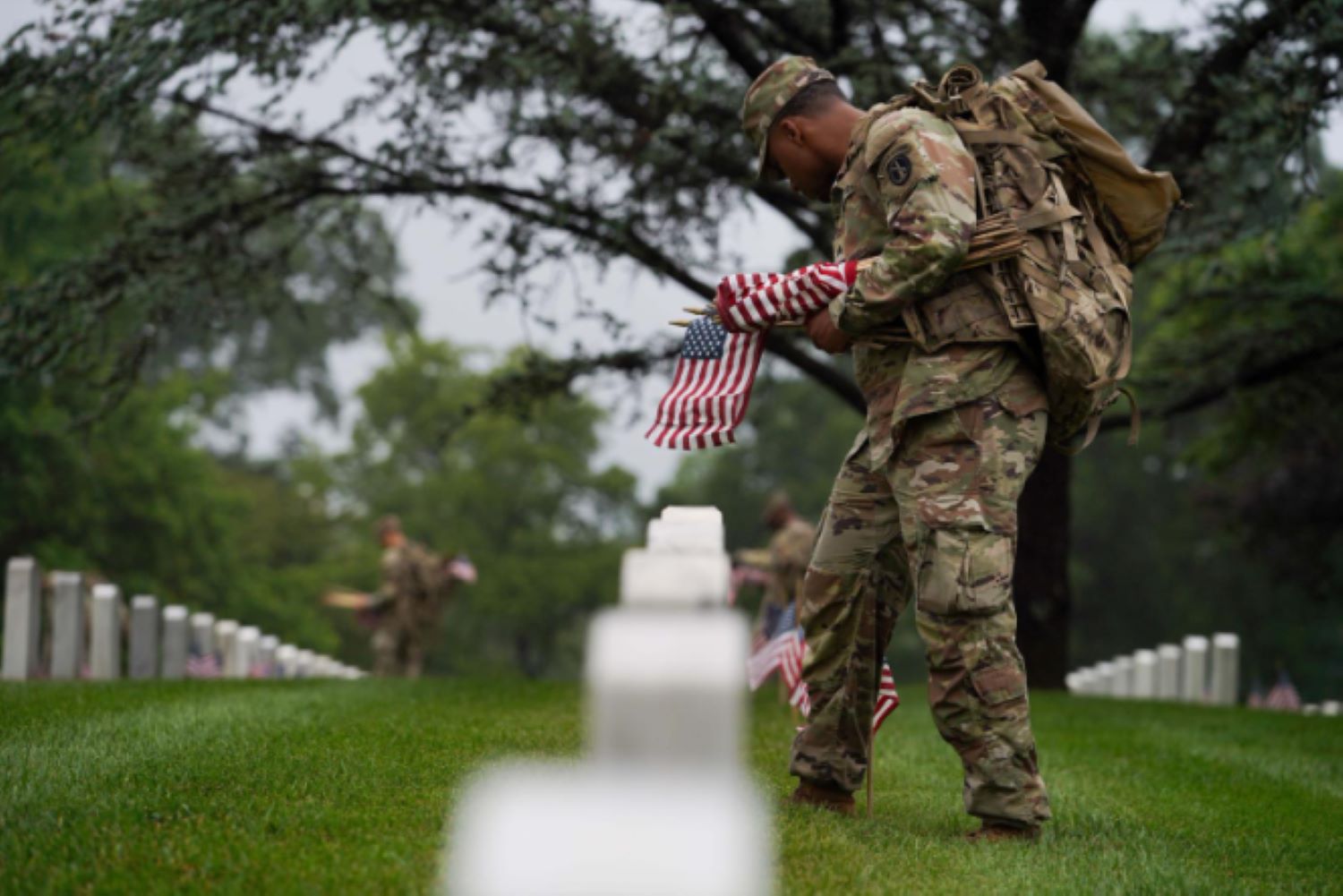 A soldier places a flag at a gravestone